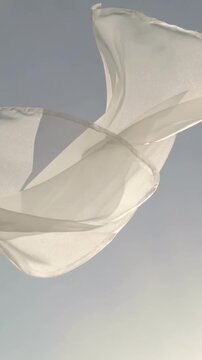 Vertical video: Billowing semi-sheer fabric moving across pale sky from wind, showing seam backlit