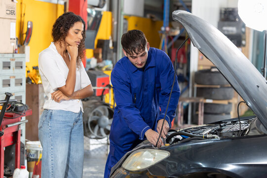 Mechanic checks car engine while customer looks on inside auto repair shop