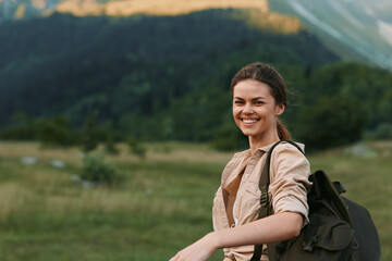 Obraz premium Woman outdoors, smiling with backpack, sunlit moment, relaxed posture, nature backdrop, grassy field, distant mountains, hiking vibe, cheerful lifestyle, fresh air