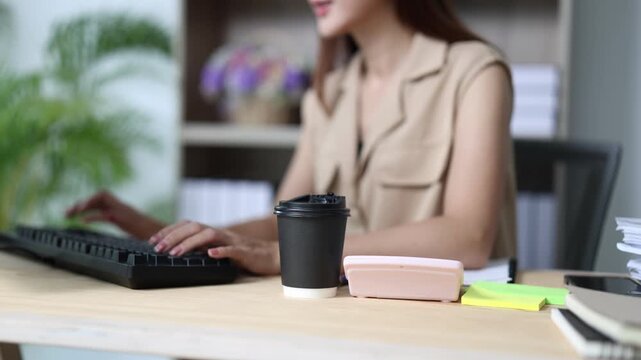 Focused businesswoman typing on a computer keyboard in a modern office while working on a project with a cup of coffee on her desk, showcasing concentration and productivity