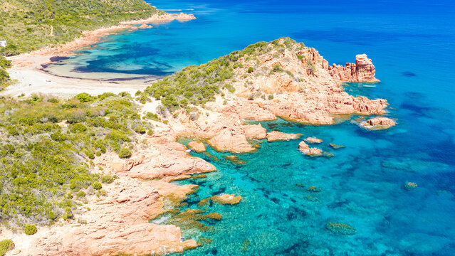 Aerial drone view of the Marina di Gairo coastline, Sardinia. Turquoise Mediterranean waters meet striking red granite cliffs, creating a wild and unspoiled coastal landscape.
