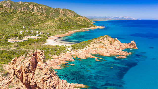 Aerial drone view of the Marina di Gairo coastline, Sardinia. Turquoise Mediterranean waters meet striking red granite cliffs, creating a wild and unspoiled coastal landscape.