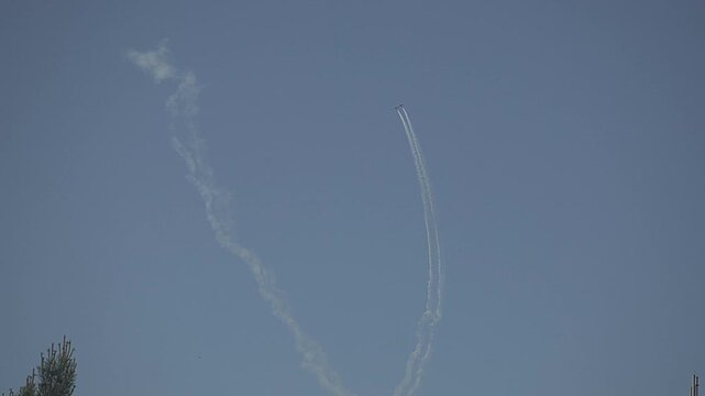 Close-up video captures arc-shaped condensation trails left by aerobatic aircraft performing a loop-the-loop maneuver. White smoke lines form a loop against a solid grey cloudy sky under natural dayli