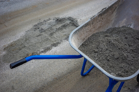 Metal wheelbarrow with cement mixture near patched asphalt pothole on suburban road. Concept: road repair