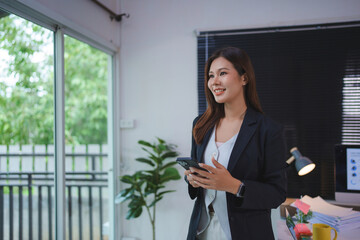 Fototapeta premium Smiling young asian businesswoman using smartphone in office