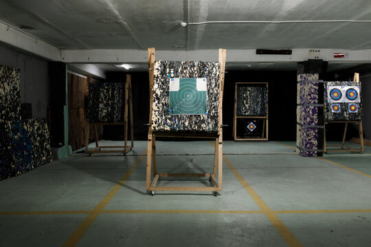 Wide photo of archery shooting target stands inside indoor range facility. Wooden easels with paper marks, concrete floor with yellow line marking, club training hall basement background, precision ex