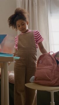Vertical video of African American child packing notebooks and school supplies into backpack. Clip perfect for back-to-school commercials and educational marketing