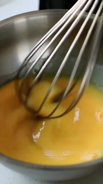 Vertical video: Entering right, metal whisk stirring beaten egg in steel bowl on counter, blending