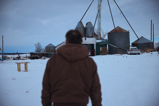 Man Walks Towards Grain Storage in Winter Landscape Near Farm