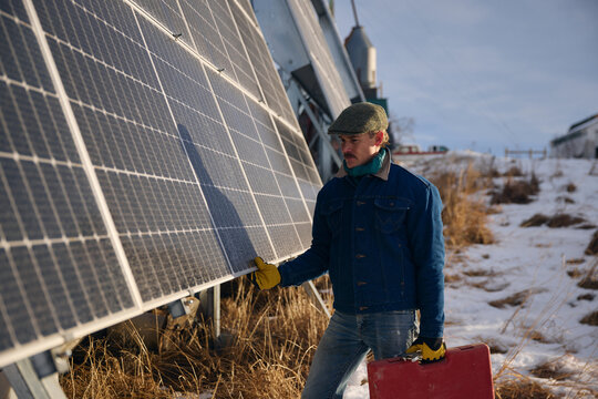 Worker Inspects Solar Panels at Snowy Field in Winter Afternoon