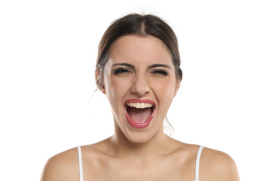 Studio portrait of happily surprised brunette woman with glamorous makeup, open mouth and white top on white background.