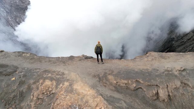 Aerial view of woman standing at the rim of Mount Bromo volcano crater surrounded by rising steam in East Java, Indonesia. Dramatic travel and adventure scene showcasing the raw power of nature.