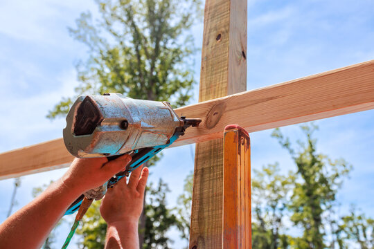 Builder operates air nail gun to secure wood beams at construction location