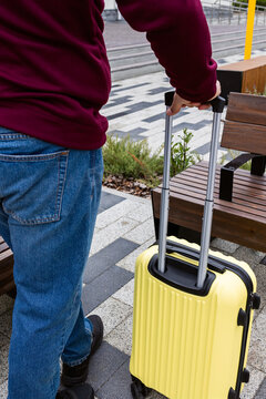 A man stands with a yellow suitcase next to the benches.