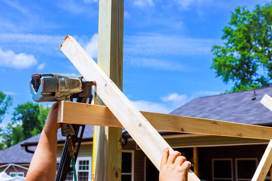 Worker assembling wooden frame with pneumatic nailer during outdoor shed construction project,