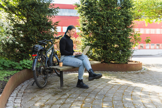 Digital nomad woman working on laptop in city park with e-bike