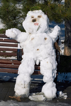 Funny melting snowman sitting on park bench with bottle in sunlight