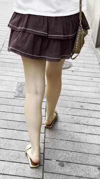 Mujer andando con sandalias, falda y bolso de espaldas en verano desde atr&aacute;s piernas pies chanclas woman walking skirt and sandals from behind 