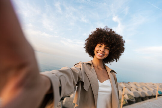 Happy black woman taking selfie at coastline