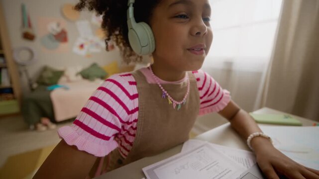 African American child wearing headphones typing on laptop and talking during online lesson. Ideal for promoting e-learning platforms, educational software, and remote school programs