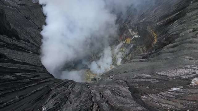 Aerial view of Mount Bromo crater in East Java, Indonesia, with thick volcanic steam rising from the caldera. Dramatic volcanic landscape showcasing geothermal activity and the raw power of nature.