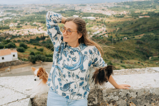 Woman with flowing hair posing beside two small dogs on scenic v