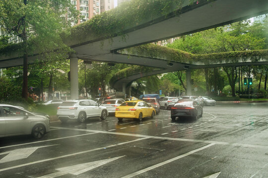 Cars travel on a busy road under a green overpass in a city 