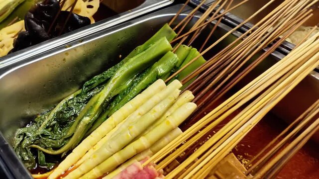 Steaming skewered Chinese street food in spicy broth at a bustling night market, featuring offal, vegetables, and tofu skin on bamboo sticks