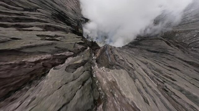Cinematic FPV drone flight descending into Mount Bromo crater in East Java, Indonesia. Volcanic steam rises from active fumaroles surrounded by rugged volcanic terrain.