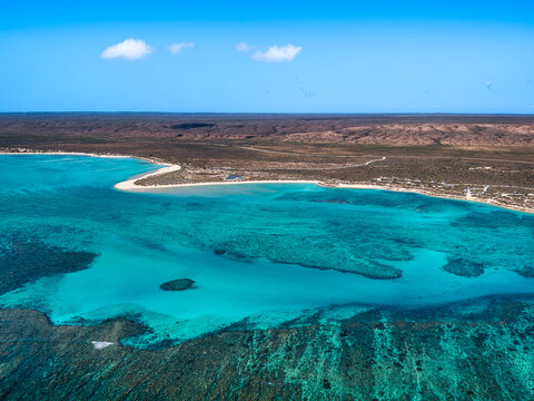 Aerial view of the turquoise waters and coral reef formations of the Ningaloo Reef, with the arid coastline and sandy beach in the background, Ningaloo, Western Australia, Australia.