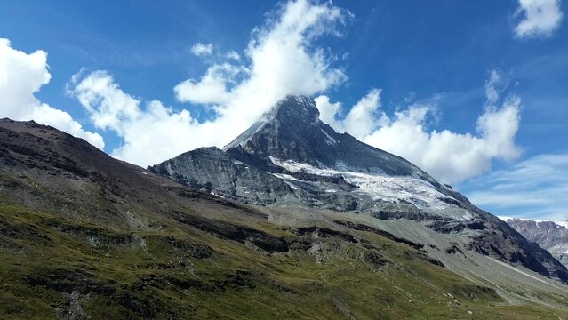 Aerial view of the Matterhorn Glacier and the iconic rocky peak of the Matterhorn under a bright blue sky with scattered clouds in Zermatt, Valais, Switzerland.