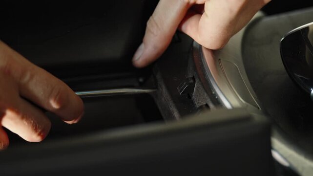 Hands removing silver trim panel from car console with tool