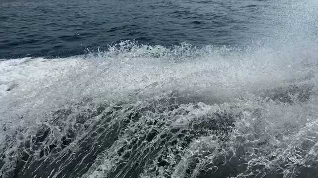 Foaming waves near the side of the ship. Close-up view of water splashing alongside a moving boat at sea, creating dynamic foam and wave patterns. Summer vacation shot.