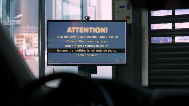 A digital screen inside a smart parking facility shows safety instructions before vehicle dropoff. The scene reflects modern parking technology, automation and secure user guidance.