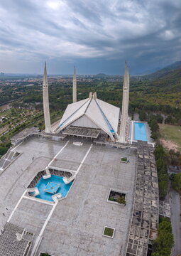 Aerial view of Faisal Masjid with its iconic tent-shaped prayer hall, four slender minarets, and blue reflecting pools set against lush green hills in Islamabad, Islamabad Capital Ter, Pakistan.