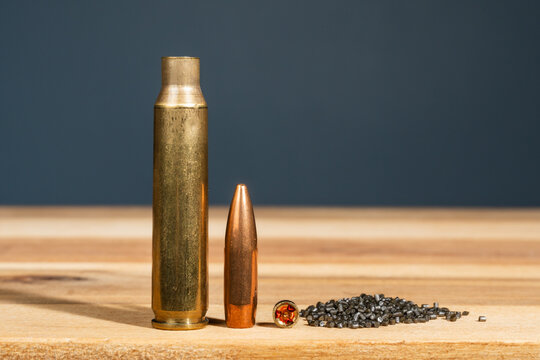 Close up of ammunition components including brass cartridge case rifle bullet small primer and smokeless gunpowder granules on wooden workbench for custom handloading process