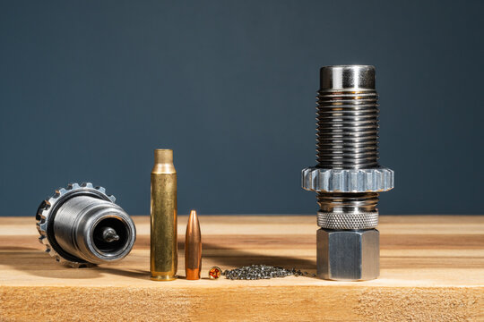 Ammunition reloading die set with brass cartridge case bullet primer and gunpowder components for precision handloading process on wooden workbench in studio