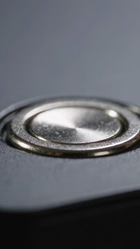 Vertical video: Coming thumb pressing, compressing then releasing metal button in studio closeup