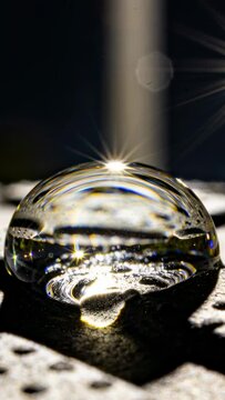 Vertical video: Hitting beam making droplet bending light on dark pitted base, showing flare
