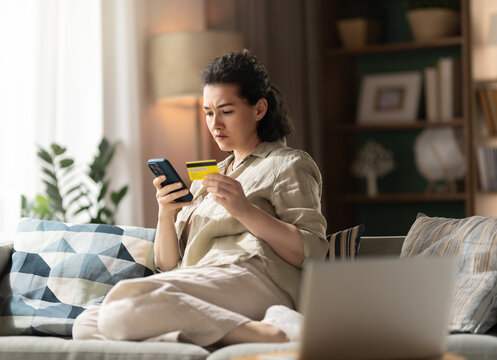 Concerned Woman Holding Credit Card and Phone at Home