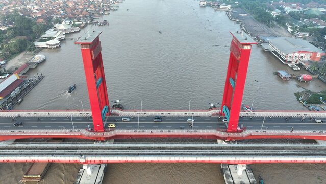 Aerial view of the iconic red Ampera Bridge spanning the Musi River with traffic and boats in Kecamatan Seberang Ulu I, Sumatera Selatan, Indonesia.