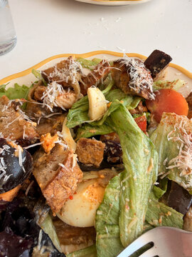 Fresh mixed salad bowl with romaine lettuce, grilled chicken, avocado, croutons, tomatoes, cheese, nuts, and creamy dressing on white table, healthy lunch meal served from above
