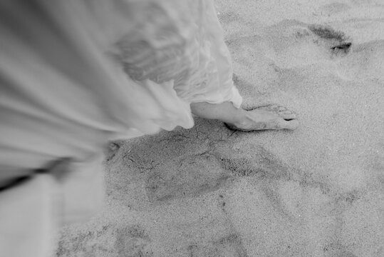 Bare foot stepping through soft beach sand with flowing fabric and gentle blur in monochrome close up, creating serene abstract texture, coastal mood, and quiet sense of movement
