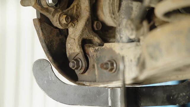 Mechanic hand using wrench to unscrew bolt on car suspension steering knuckle close up