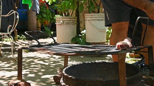 Parrillero acomodando carne vacuna sobre parrilla durante preparaci&oacute;n de asado argentino tradicional