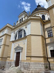 Obraz premium Baroque Catholic church with yellow facade dome and statues against blue sky in Sarajevo