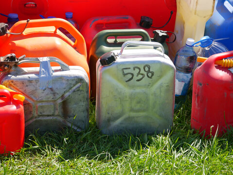 Metal and plastic canisters filled with fuel on green grass. Multiple gasoline containers stored for emergency use. Industrial supply and energy storage concept in outdoor environment.