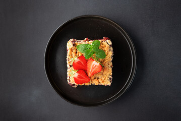 Sweet homemade pie with strawberry jam, decorated with fresh strawberries and aromatic herbs on black ceramic plate, on dark stone background top view. © Iryna