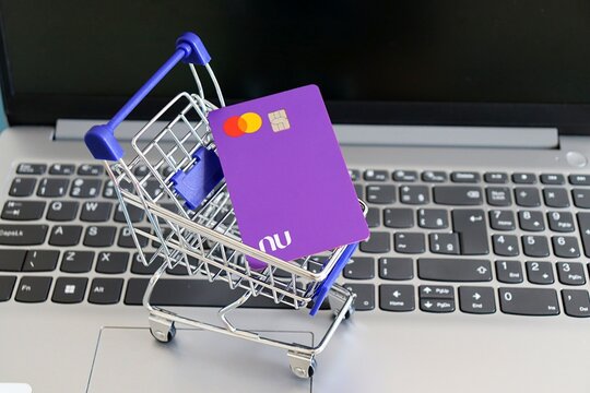 Salvador, Brazil - June 24, 2026: Nubank credit card inside a miniature supermarket shopping cart on top of a laptop keyboard. Online shopping and digital banking. Brazilian Nubank.