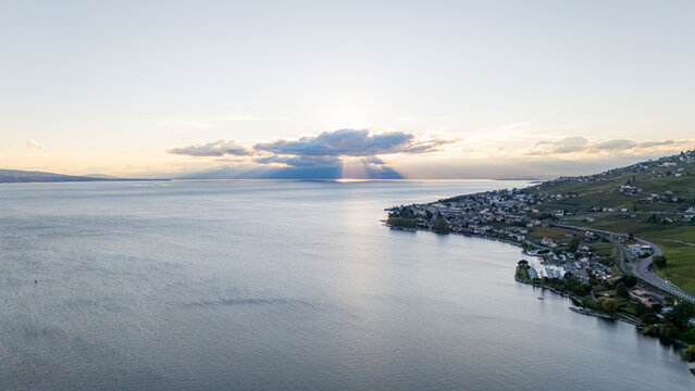 Aerial view of Epesses vineyards along the shores of Lake Geneva at sunset, with sunbeams breaking through clouds over the water in Bourg-en-Lavaux, Vaud, Switzerland.